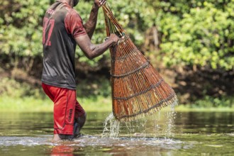 Fisherman lifting the basket out of the water. Water trips down the basket. He uses the basket for