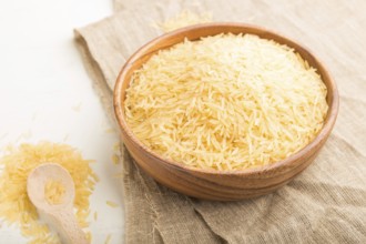 Wooden bowl with raw golden rice and wooden spoon on a white wooden background and linen textile.