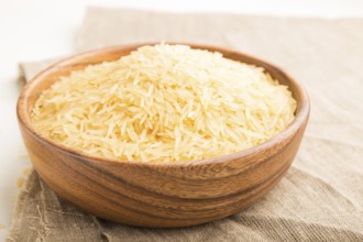 Wooden bowl with raw golden rice and wooden spoon on a white wooden background and linen textile.