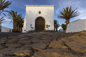 White chapel with palm trees and cobblestones in the foreground under a blue sky, Canary Islands,