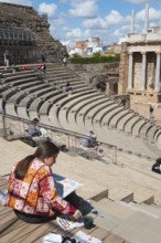 Woman painting a Roman theatre outdoors on a historical site, surrounded by stairs under a blue