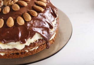 Homemade chocolate cake with milk cream, caramel and almonds on white wooden background. close up