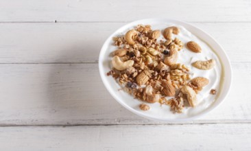 White plate with greek yogurt, granola, almond, cashew, walnuts on white wooden background. close