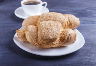 Two croissants with cup of coffee on white plate on black wooden background. closeup