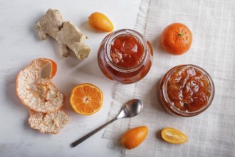 Tangerine and kumquat jam in a glass jar with fresh fruits on white wooden background. Homemade,