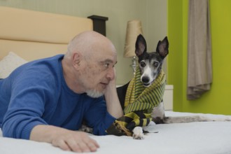 A mature gentleman, accompanied by his greyhound companion, poses for the camera from the comfort