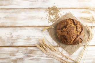 Fresh homemade golden grain bread with ears of wheat and rye on white wooden background and linen