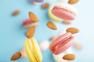 Multicolored flying macaroons and almonds eggs frozen in the air on blurred blue background. top