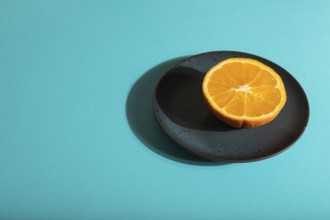 Ripe cut orange on blue ceramic plate on blue pastel background. Side view, copy space, hard light.