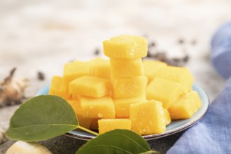 Dried and candied mango cubes on blue plate on brown concrete background and linen textile. Side