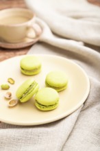 Green macarons or macaroons cakes with cup of coffee on a brown concrete background and linen