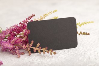 Black paper business card mockup with purple astilbe flowers on gray concrete background. Blank,