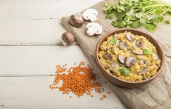 Lentils porridge with champignons and coriander in a wooden bowl on a white wooden background and