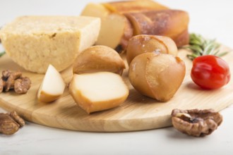 Smoked cheese and various types of cheese with rosemary and tomatoes on wooden board on a white