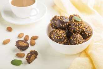 Chocolate caramel ball candies with almonds and a cup of coffee on a white wooden background and