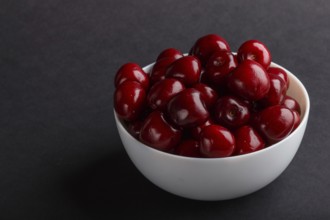 Fresh red sweet cherry in white bowl on black background. side view, close up