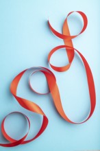 Red coral ribbon on a blue pastel background. Celebration concept. Top view, close up, flat lay