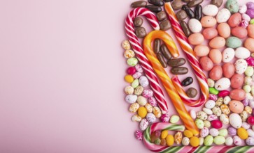 Colorful multicolored candies on a pink pastel background. Christmas cane, chocolate eggs, caramel