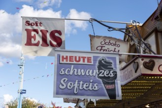 Advertising sign for black soft ice cream on a fairground with blue sky in the background,