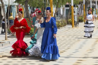 Five woman in different colourful flamenco dresses, with flowers in their hair, strolling on a