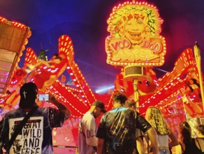 People in front of the illuminated carousel Voodoo Jumper at night, Cranger Kirmes, Herne, Ruhr