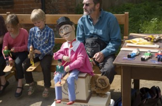 Man and children operating a traditional wooden jig doll dancer during a country folk event at