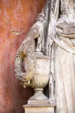 White angel, hand holding a wreath of flowers on an urn, detail of a stone statue, weathered,