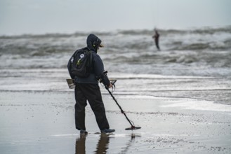 Treasure hunter, man with metal detector on the beach, dark storm clouds, autumn at the North Sea