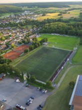 Aerial view of a village with a sports field, football pitches and tennis courts, surrounded by