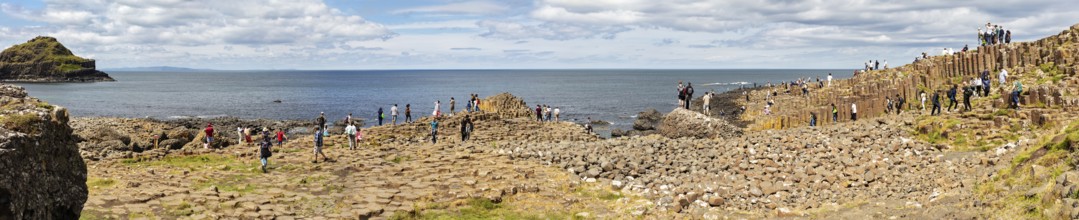 Panorama of people on basalt columns with sea view under cloudy sky, Giant Causeway