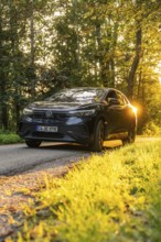 Car on forest road with setting sun in the background, harmonious atmosphere, electric car, VW ID5,