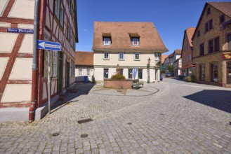 Running fountain with half-timbered house and historical buildings under a cloudless blue sky on