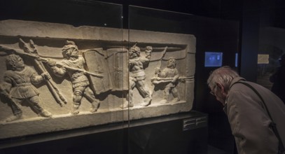 Visitor looking at tomb relief fragment showing gladiators fighting in ancient Rome in the