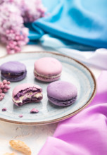 Purple macarons or macaroons cakes with cup of coffee on a white concrete background and