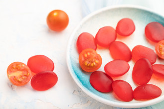 Jelly tomato candies on white concrete background and blue linen textile. close up, side view,