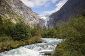 A river flows in front of the melting Kjenndalsbreen glacier between steep mountains through a