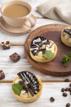 Sweet tartlets with chocolate and cheese cream with cup of coffee on a white wooden background and