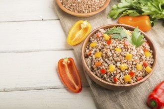 Buckwheat porridge with vegetables in wooden bowl on a white wooden background and linen textile.