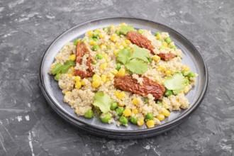 Quinoa porridge with green pea, corn and dried tomatoes on ceramic plate on a gray concrete