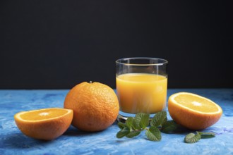 Glass of orange juice with mint on a black and blue background. Hard light, contrast. Side view,