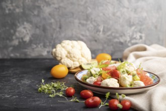 Vegetarian salad of cauliflower cabbage, kiwi, tomatoes, microgreen sprouts on black concrete