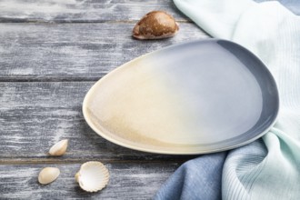 Empty blue ceramic plate on gray wooden background and blue textile. Side view, close up