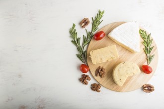 Cheddar and various types of cheese with rosemary and tomatoes on wooden board on a white wooden