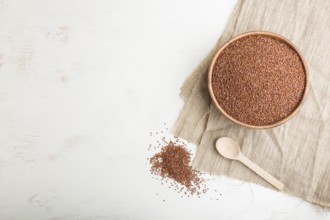 Wooden bowl with raw red quinoa seeds on a white wooden background and linen textile. Top view,