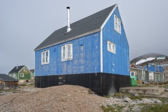 Blue house with chimney on rocky ground surrounded by colourful houses, remote Arctic Inuit