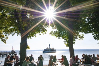 People in a beer garden under chestnut trees in Herrsching am Lake Ammer, in the background a