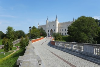 Path leads to a castle with towers and battlements, surrounded by trees and greenery, castle with