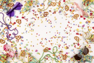 Colourful party decorations with confetti, pretzels, pearl necklaces and funny glasses on a white