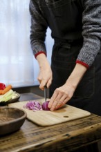 Unrecognizable man chopping red onion on a wooden cutting board in a warm kitchen