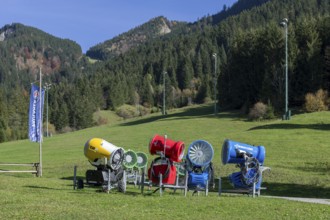 Snow cannons stand on a green meadow in front of a sunny mountain landscape, Schwangau, Ostallgäu,